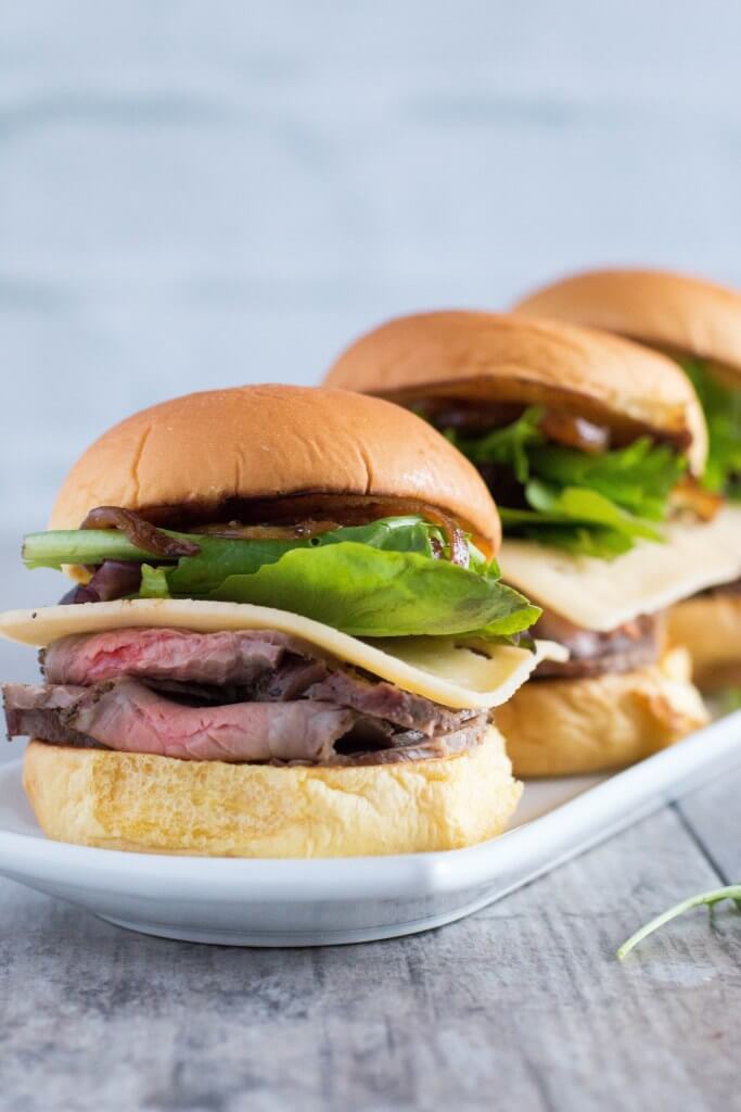 a close up of roast beef sliders on a white plate on a grey surface