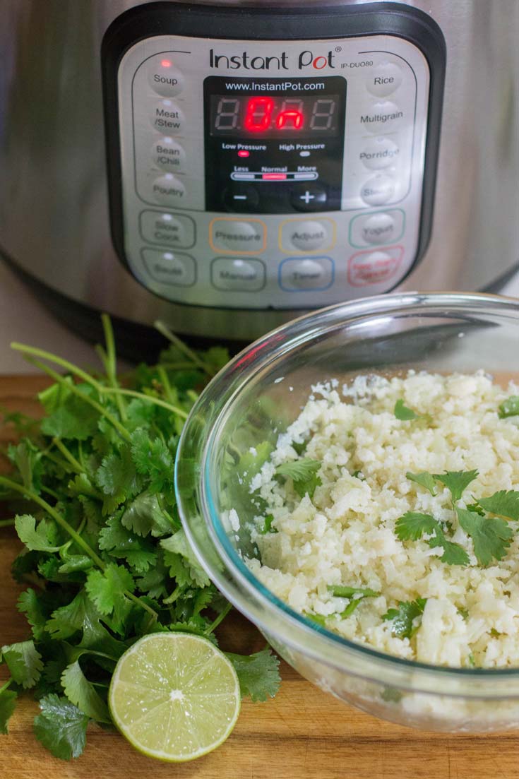 Instant Pot Cilantro Lime Cauliflower Rice in a glass bowl with a lime and cilantro.