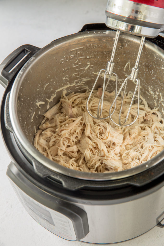 instant pot with cooked chicken breast being shredded using a hand mixer