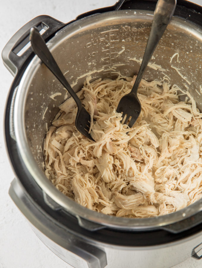 instant pot with cooked chicken breast being shredded using 2 forks