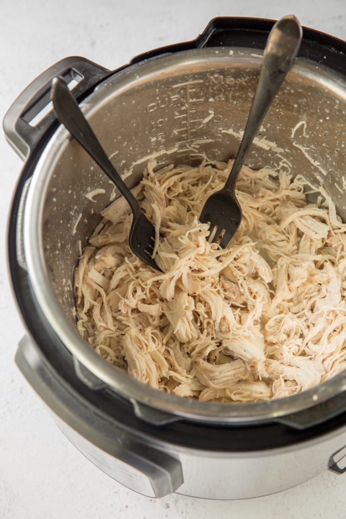 instant pot with cooked chicken breast being shredded using 2 forks