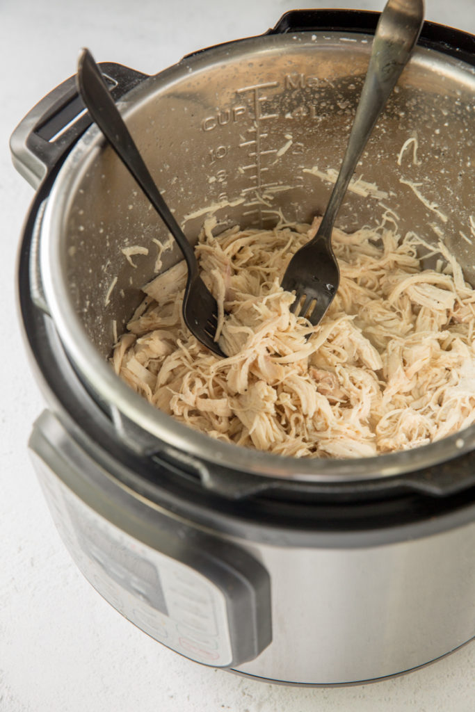 instant pot with cooked chicken breast being shredded using 2 forks