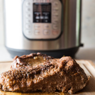 vertical image of cooked beef brisket on a cutting board with instant pot in the background