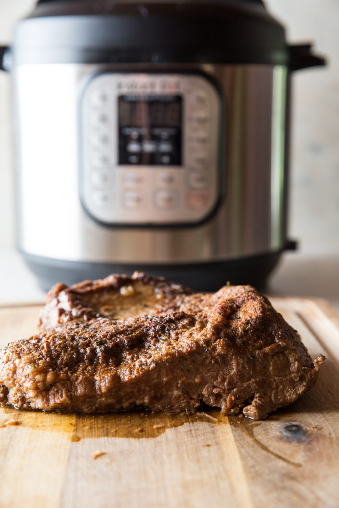 vertical image of cooked beef brisket on a cutting board with instant pot in the background