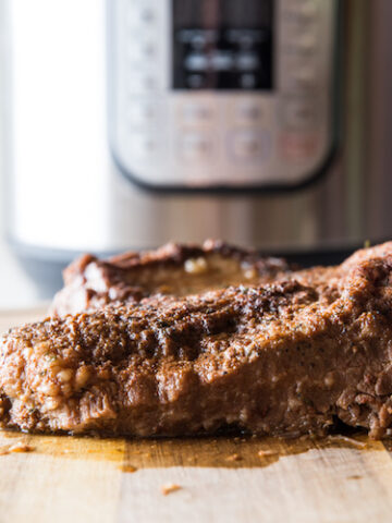 horizontal image of cooked beef brisket on a cutting board with instant pot in the background
