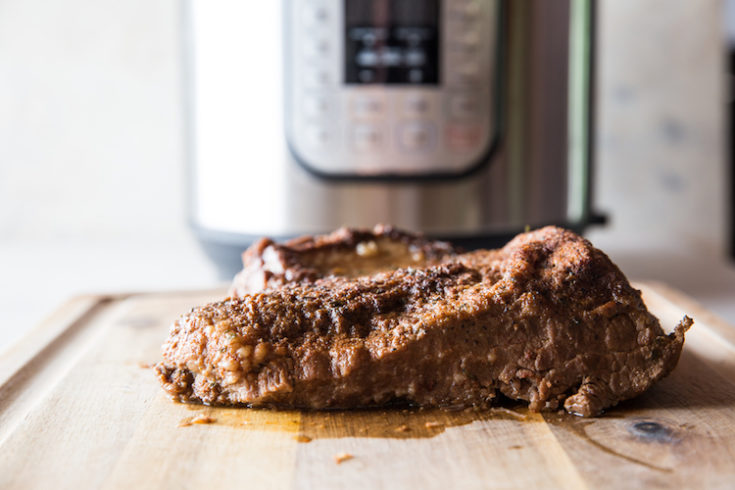horizontal image of cooked beef brisket on a cutting board with instant pot in the background