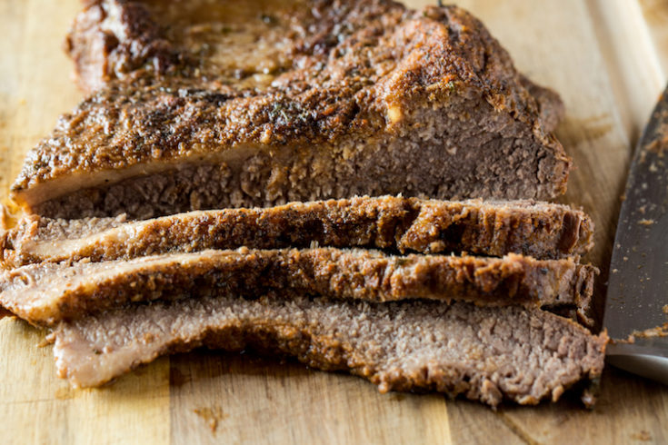 close up image of sliced cooked beef brisket on a wood cutting board