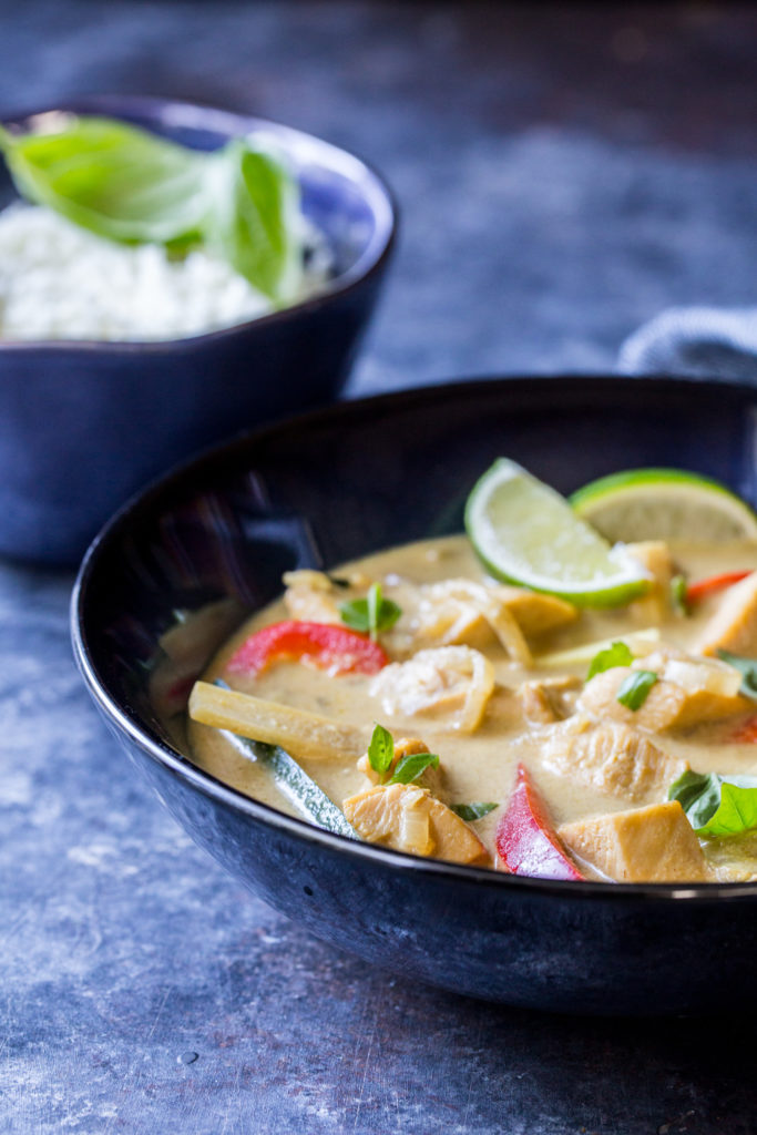 close up image of thai green curry with bell peppers and sliced limes and cauliflower rice