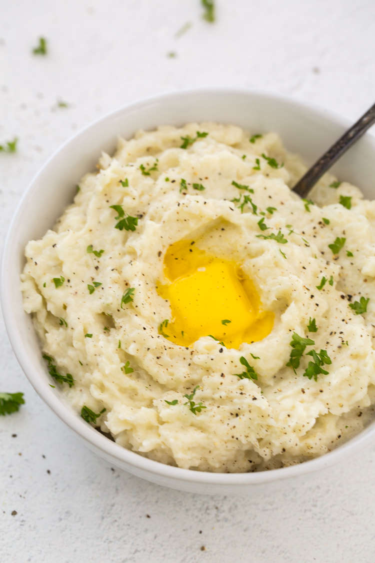 Instant Pot Mashed Cauliflower in a white bowl with a spoon, parsley, butter, salt, and black pepper.