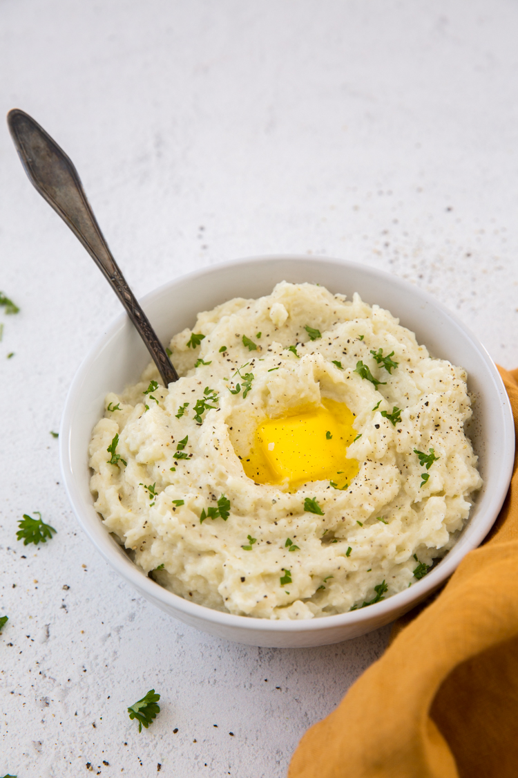 Instant Pot Mashed Cauliflower with a spoon, butter and parsley with an orange napkin