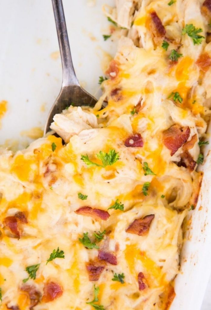 chicken with bacon and cheese throughout in a white casserole dish with the top of a silver fork showing