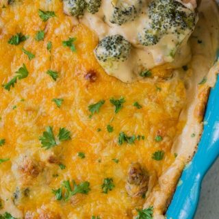 broccoli and cheese casserole in a blue baking dish with a wooden spoon