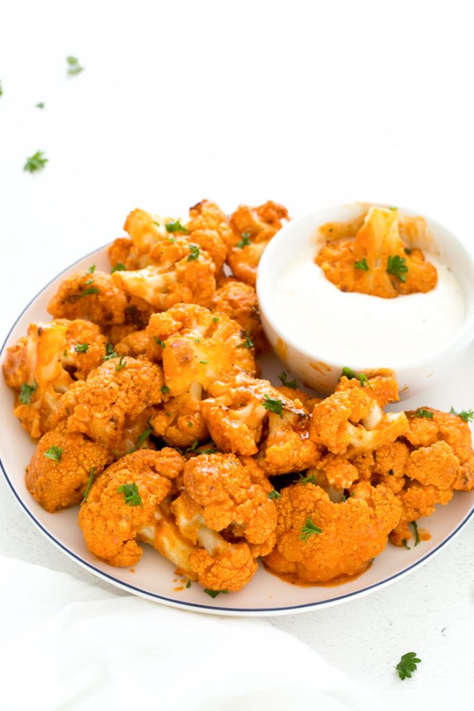 keto buffalo cauliflower on a plate with a side of blue cheese topped with parsley 