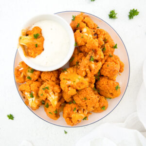 square image of keto buffalo cauliflower on a plate with a side of blue cheese topped with parsley
