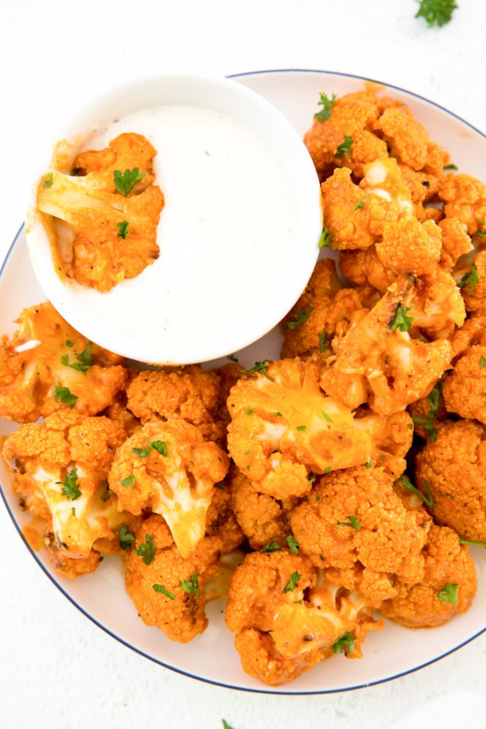 keto buffalo cauliflower on a plate with a side of blue cheese topped with parsley 