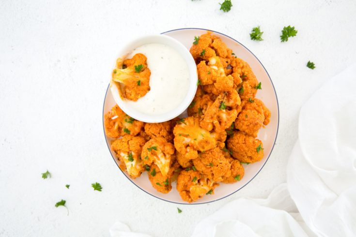 keto buffalo cauliflower on a plate with a side of blue cheese topped with parsley 