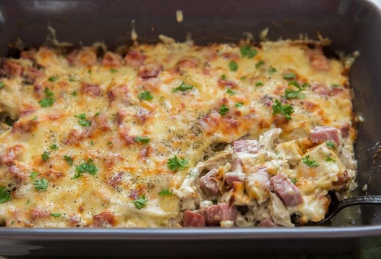 Chicken cordon bleu in a grey baking dish with a silver spoon coming out and all on top of a green towel