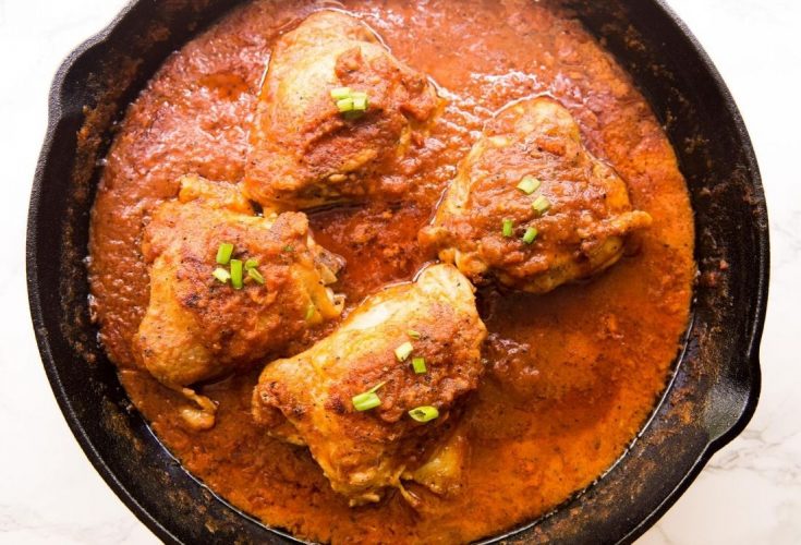 coconut milk chicken thighs in a pan surrounded and covered in a red sauce