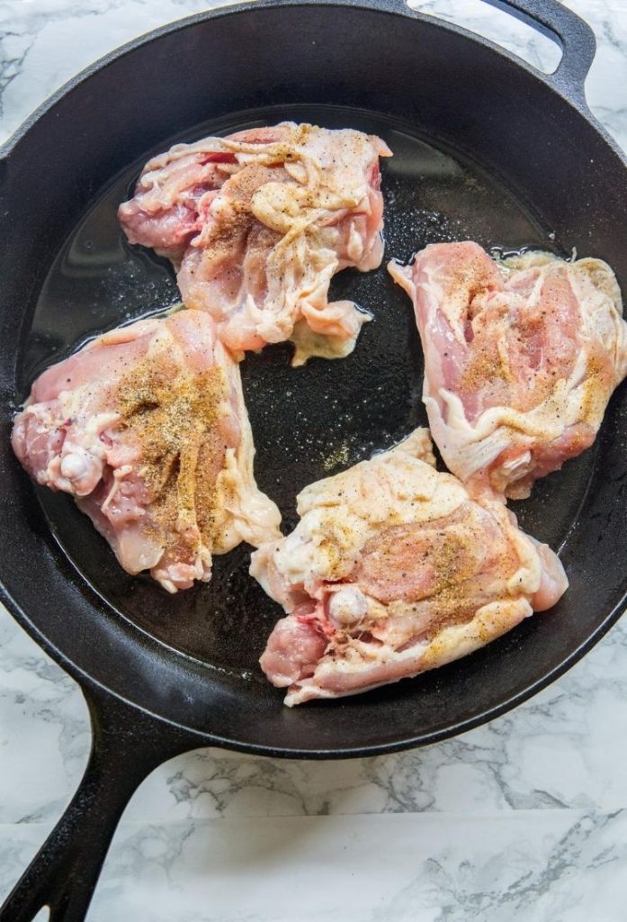 raw chicken with seasoning on top cooking in a black pan