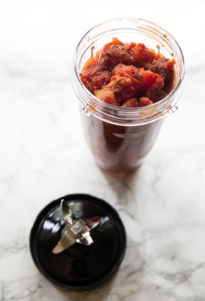 chunky red sauce in a clear cup with a black blender piece next to it