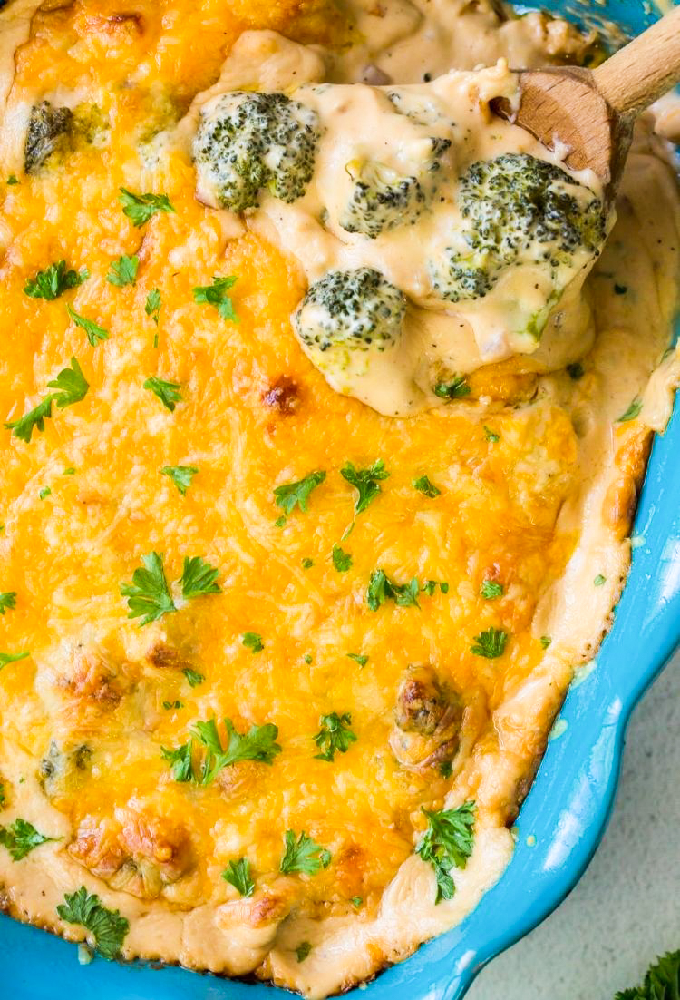 Keto Broccoli Cheese Casserole in a blue casserole dish with parsley and a wooden spoon. 