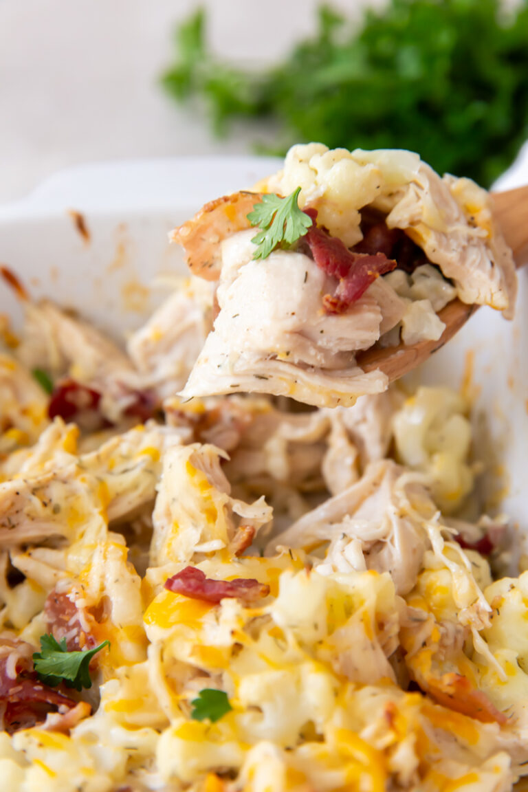 Keto Chicken Bacon Ranch with cauliflower, cheese, and parsley in a white casserole dish with a wooden spoon.