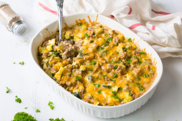 horizontal image of keto ground beef in a white casserole dish with a spoon and topped with parsley 
