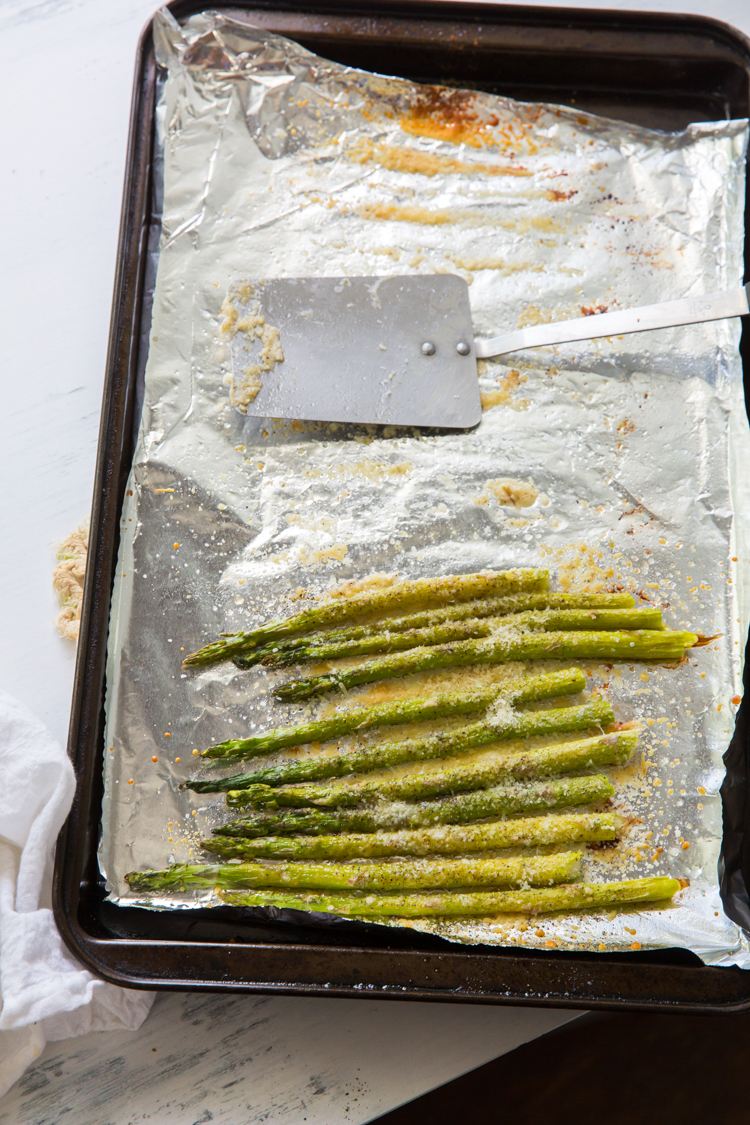roasted garlic parmesan asparagus on a cookie sheet with aluminum foil and a spatula 
