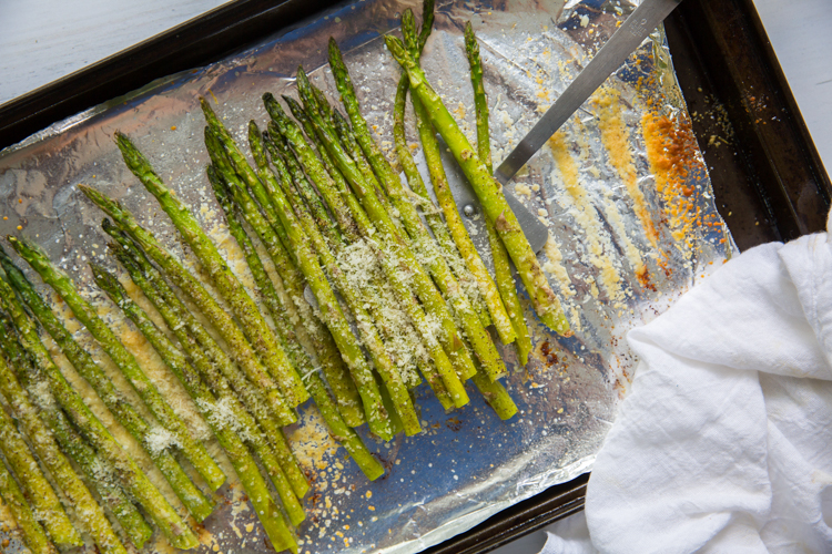 roasted garlic parmesan asparagus on a cookie sheet with aluminum foil and a spatula 