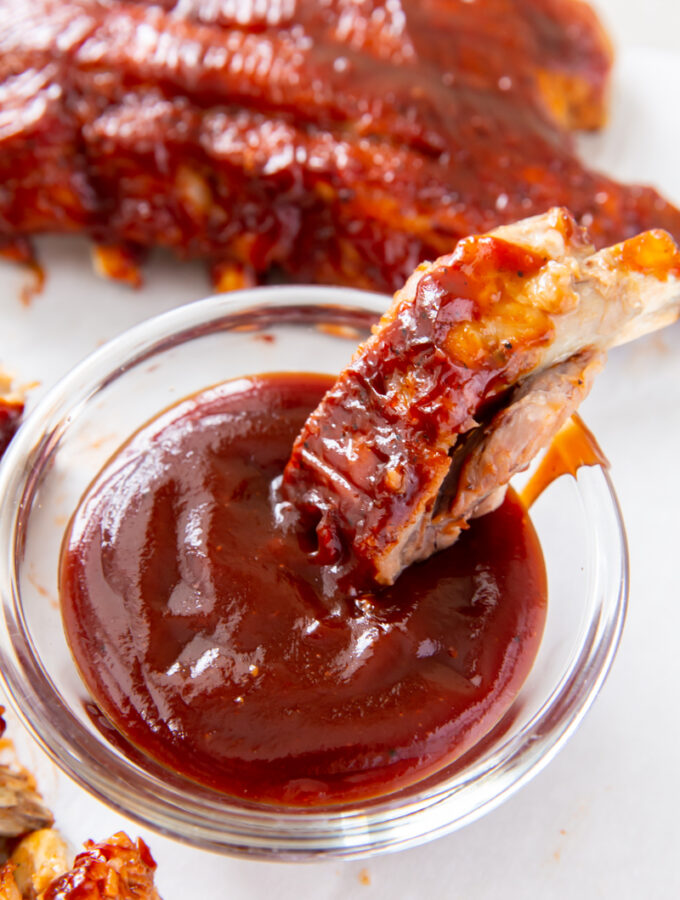 baby back rib being dipped into BBQ sauce in a clear glass container