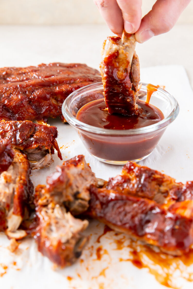 baby back rib bring dipped into a bowl of bbq sauce surrounded by more ribs
