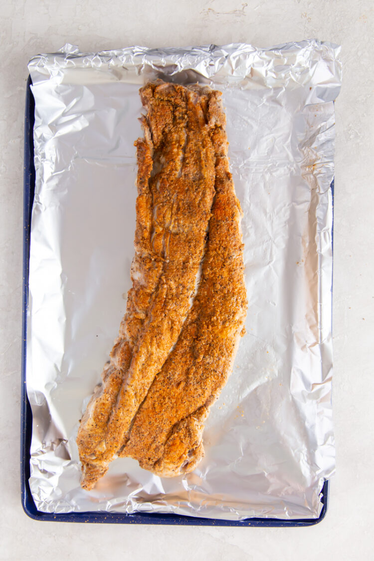 over head image of baby back ribs with dry rub on a baking sheet with aluminum foil