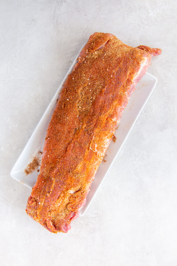 a raw rack of baby back ribs with dry rub