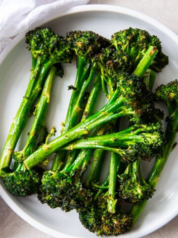 Air fried broccolini on a white plate with a white napkin on a light background.