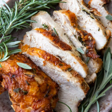 sliced turkey breast with golden brown skin with fresh sage and rosemary