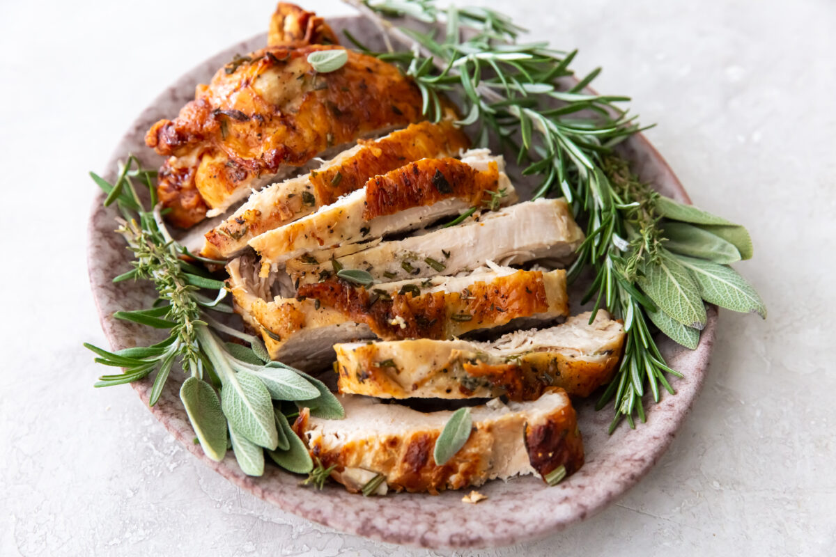 sliced turkey breast with golden brown skin with fresh sage and rosemary
