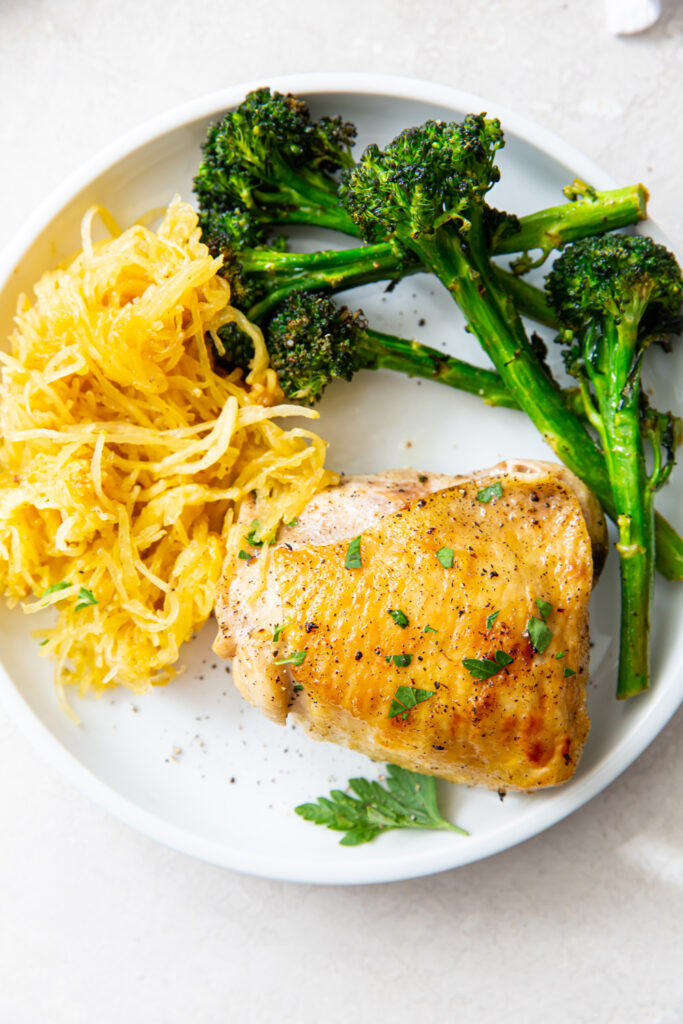 broiled chicken thigh, broccolini and spaghetti squash on a white plate