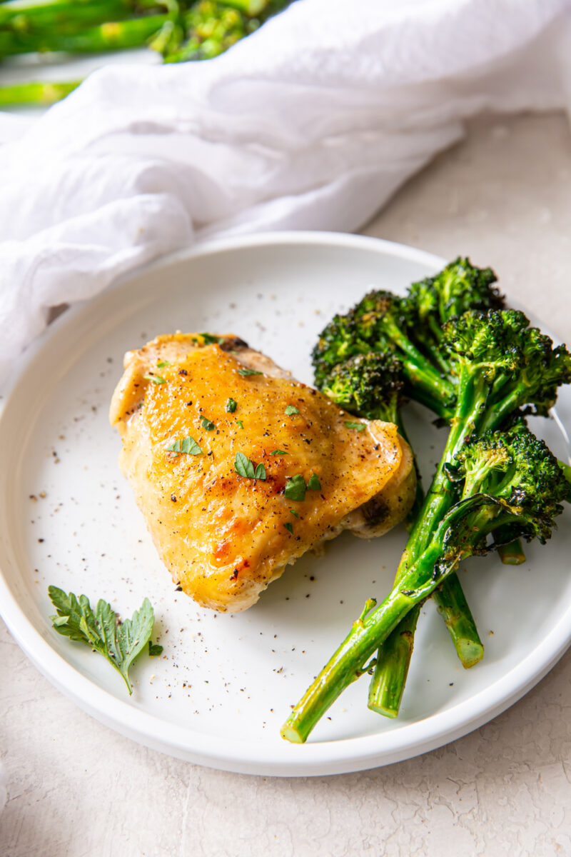 broiled chicken thigh and broccolini on a white plate