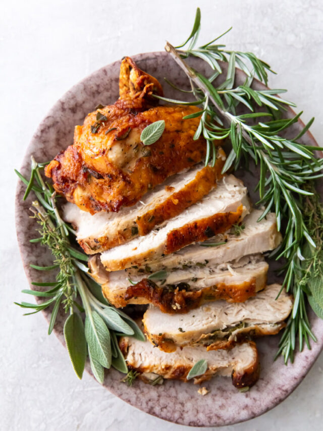sliced turkey breast with golden brown skin with fresh sage and rosemary