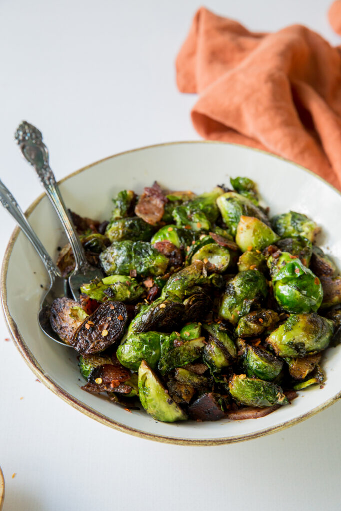 Brussels sprouts with bacon in a white bowl with silverware and a orange napkin