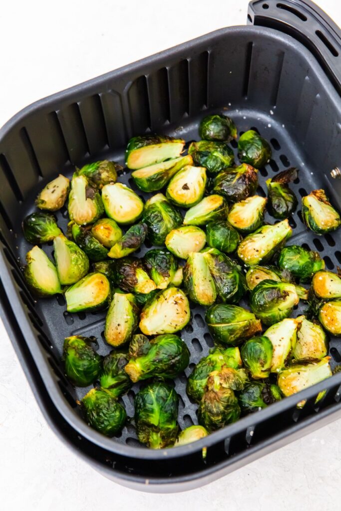 cooked halved brussel sprouts in an air fryer basket.
