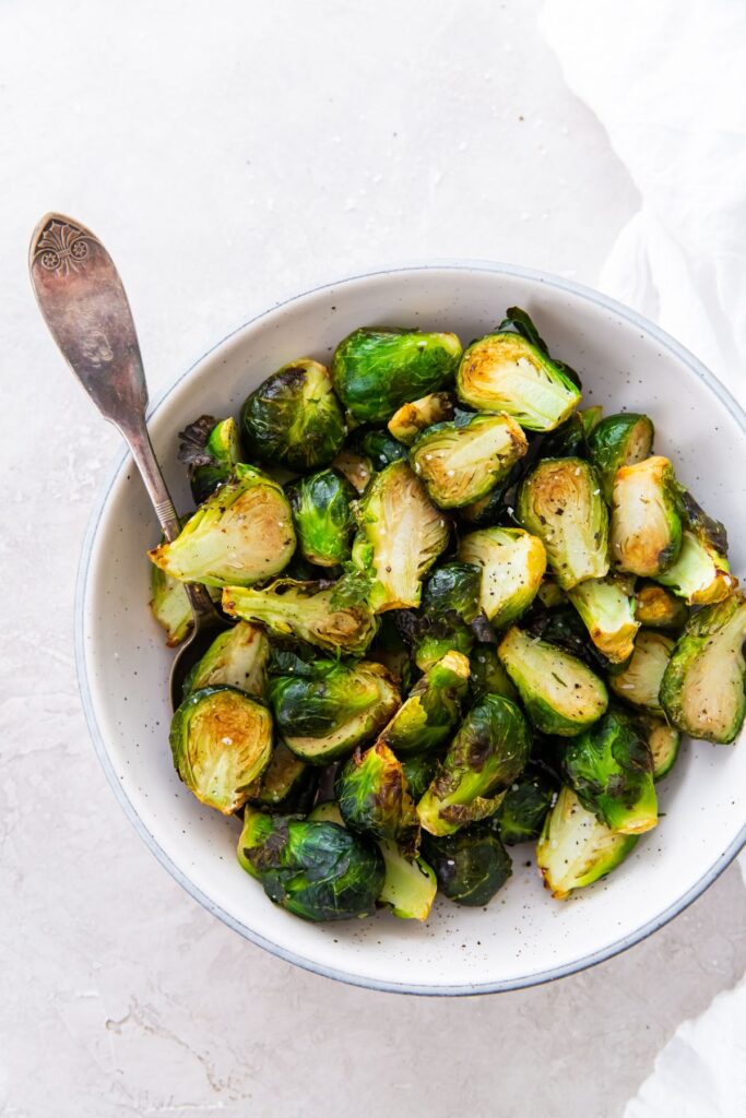 cooked Brussel sprouts in a white bowl with a spoon with a white napkin.