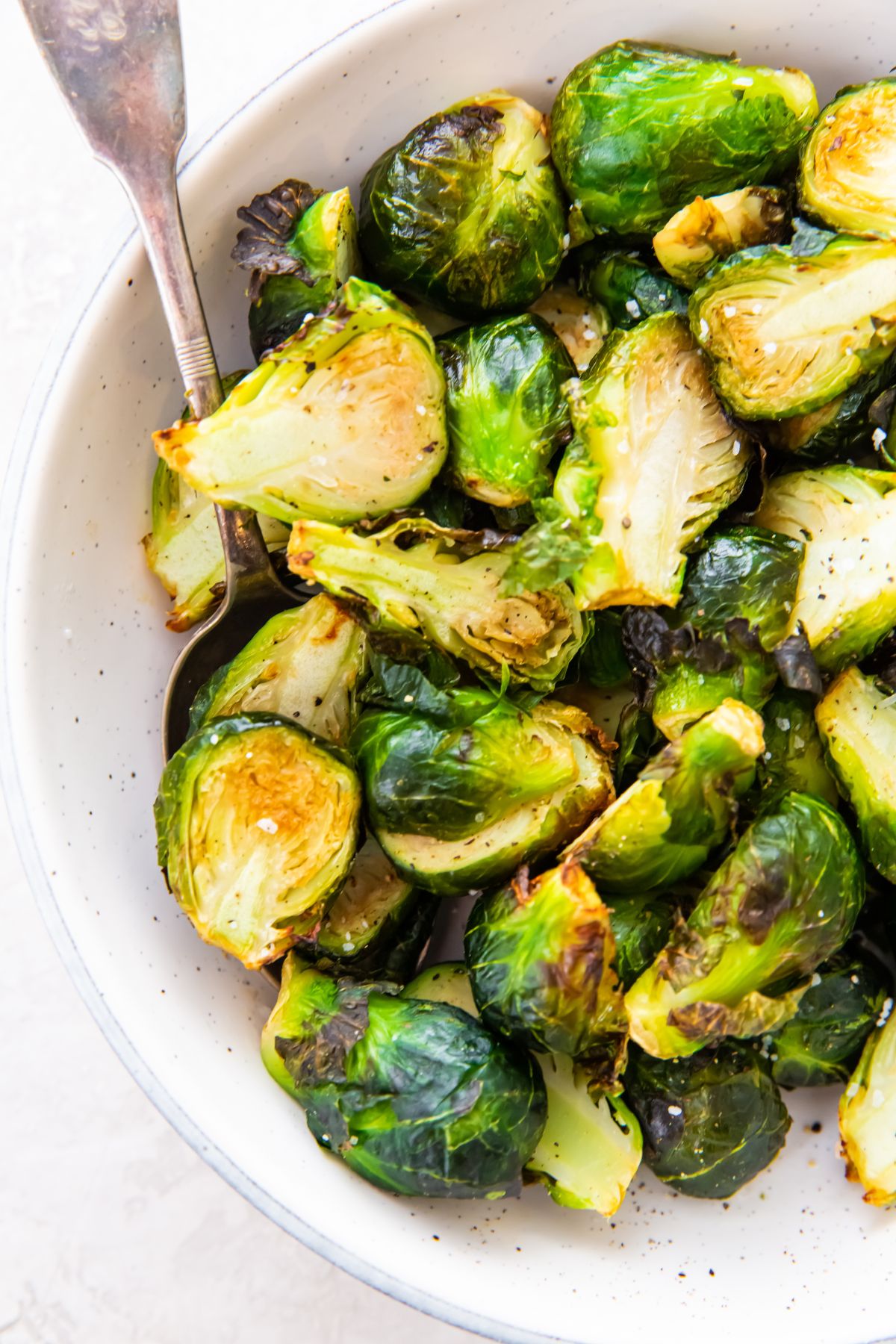 Brussel Sprouts in a white bowl with a spoon. 