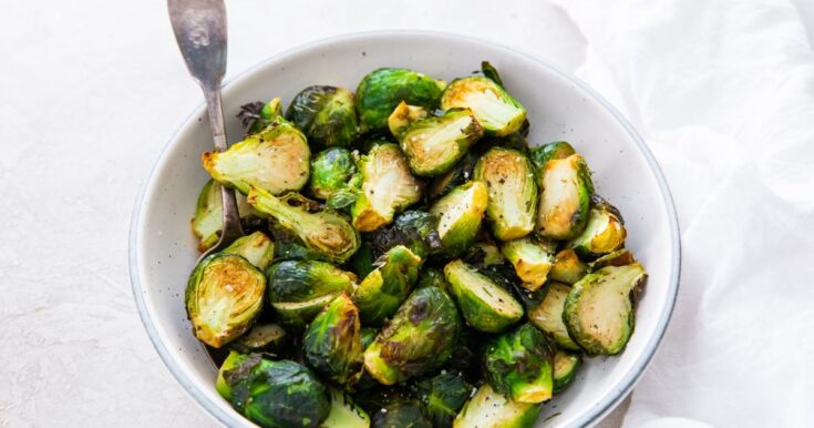 cooked Brussel sprouts in a white bowl with a spoon with a white napkin.