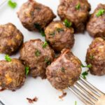 air fryer keto meatballs on a white plate being stabbed by a fork