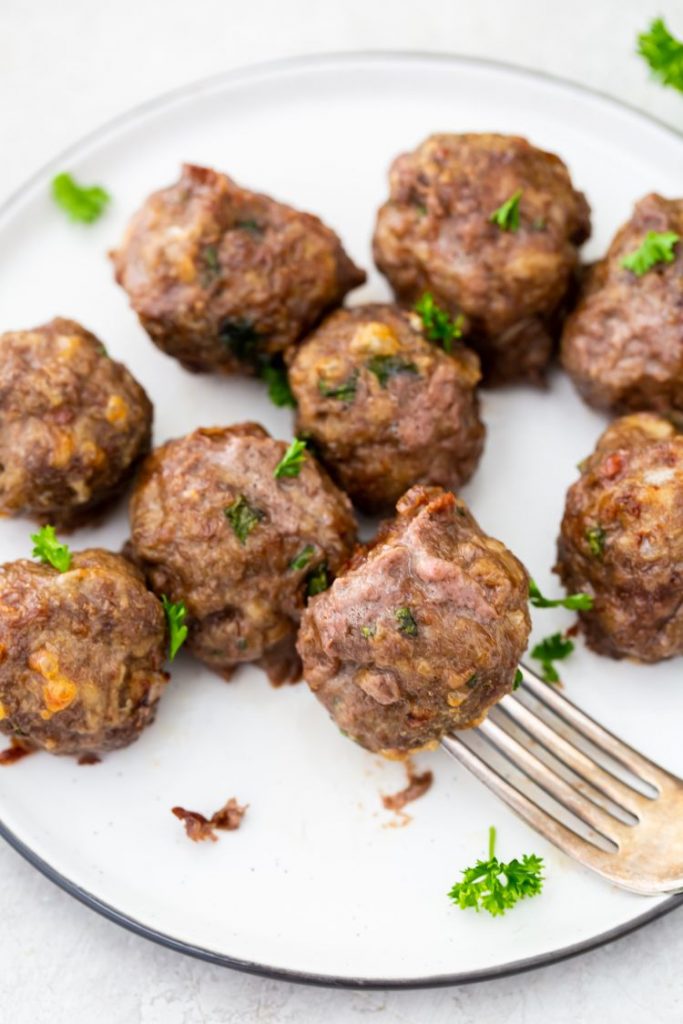 air fryer keto meatballs on a white plate being stabbed by a fork