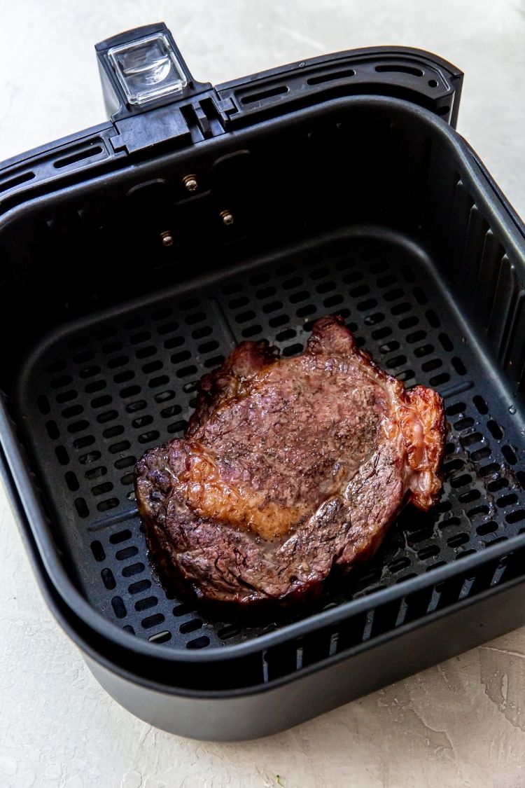 a cooked ribeye steak in an air fryer basket