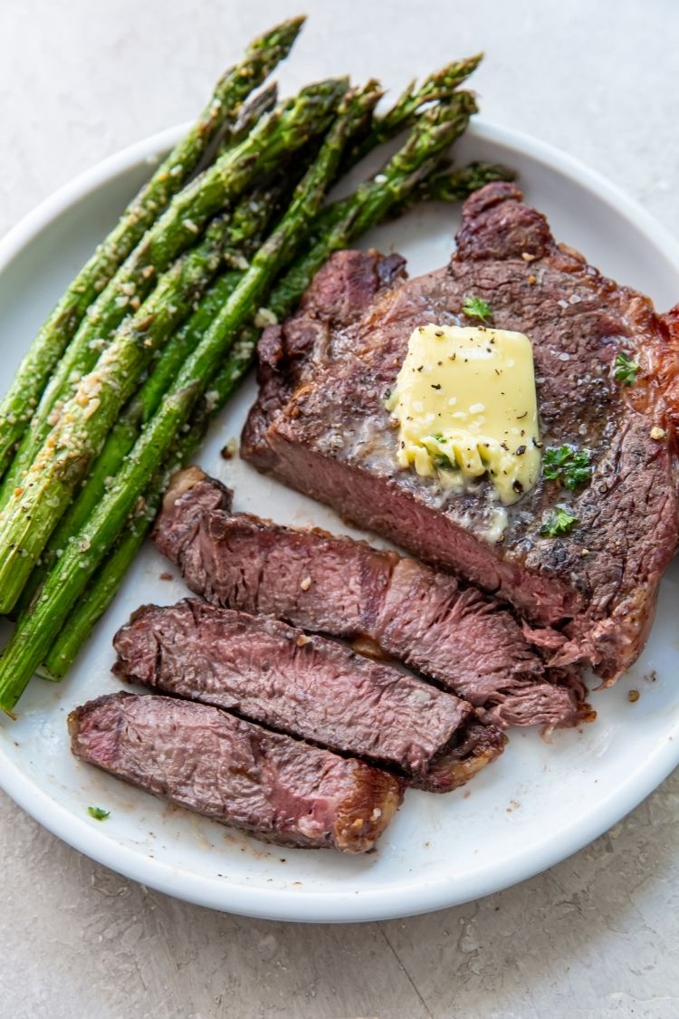juicy ribeye steak topped with butter served with asparagus