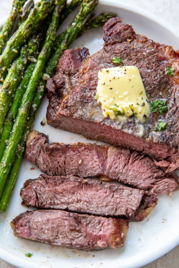 juicy ribeye steak topped with butter served with asparagus