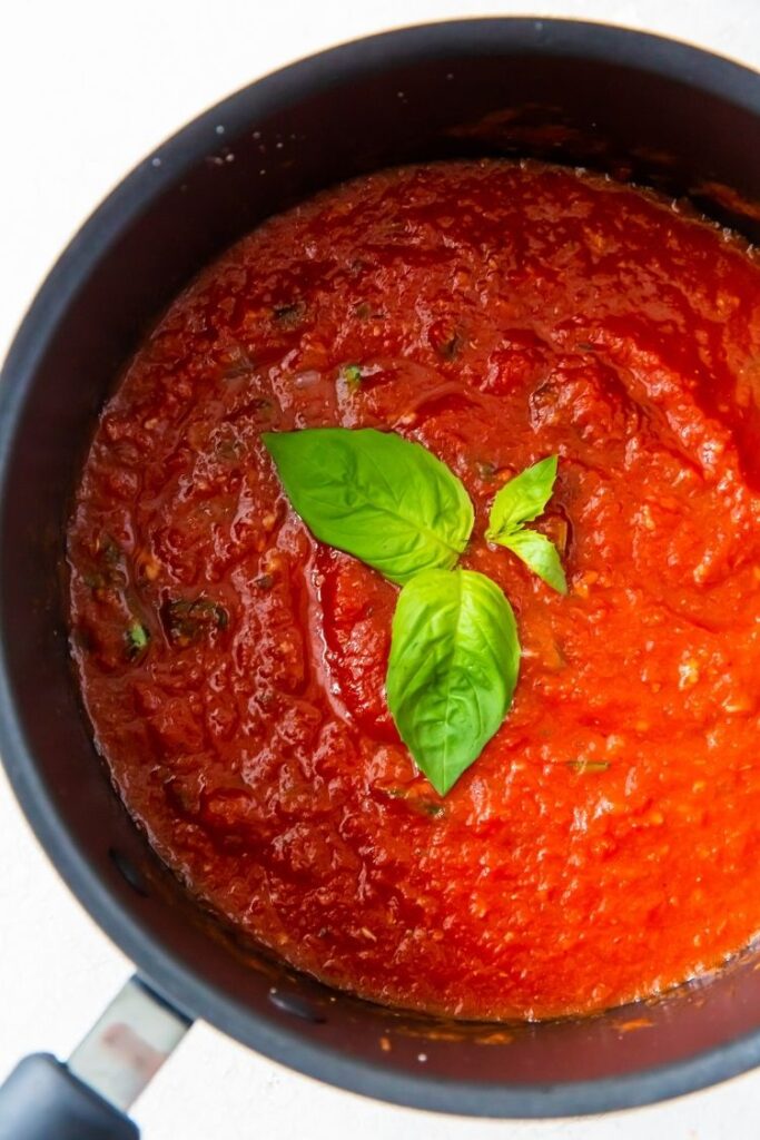 Keto spaghetti sauce in a saucepan with a piece of basil